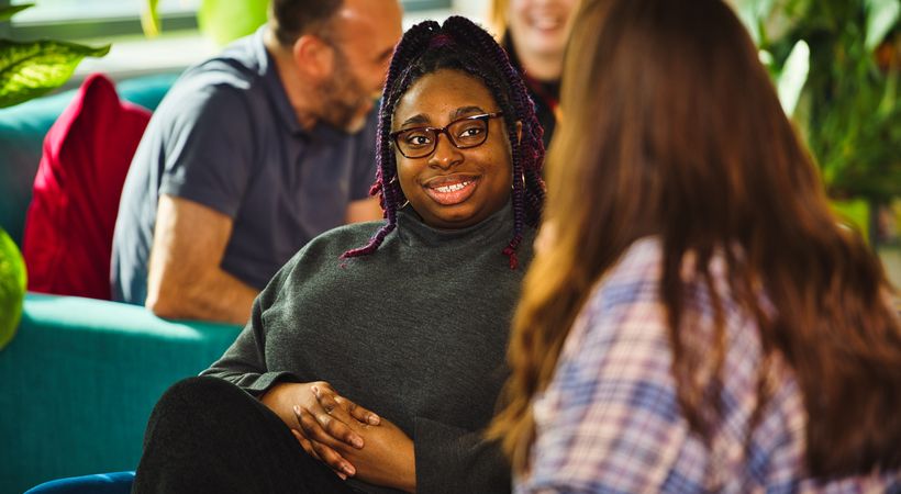 Two PSS teammates are sat in conversation. There are other teammates sat behind.